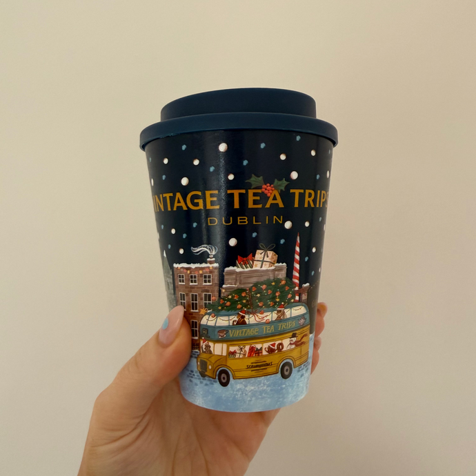 Hand holding a travel mug with 'Vintage Tea Tram Dublin' design on a plain background